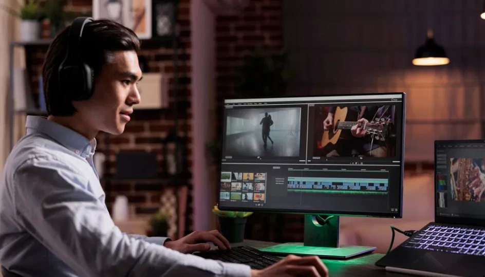 A man wearing headphones and editing a video in software on a PC