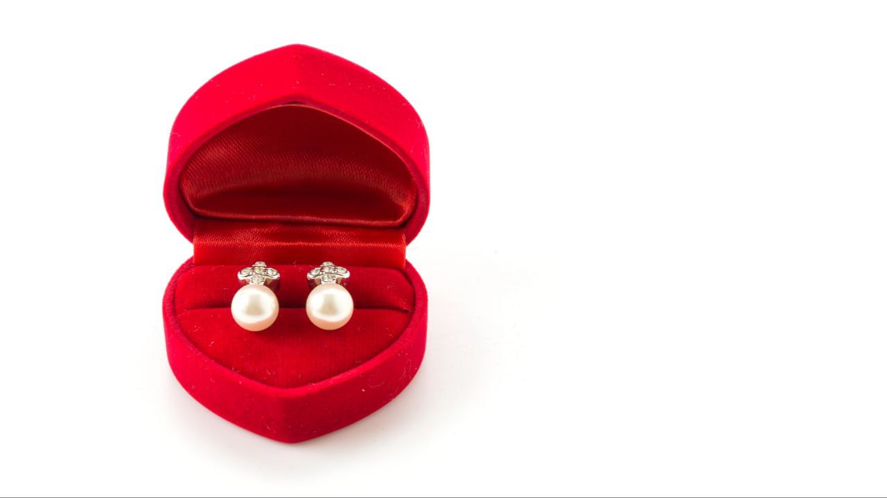 A pair of pearl earrings in a red, heart-shaped case. 