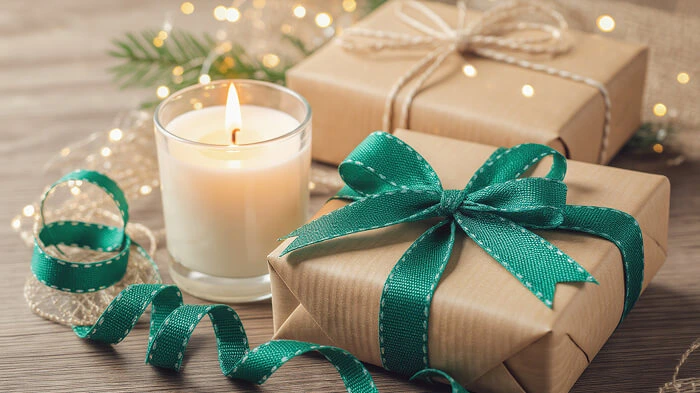Candle glowing beside wrapped gifts and bright festive ribbons.