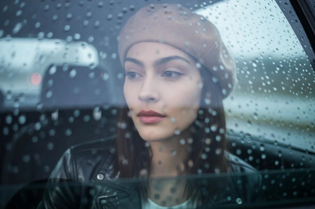 Moody rainy car portrait of a girl wearing a beige beret beside a foggy rain-covered window.