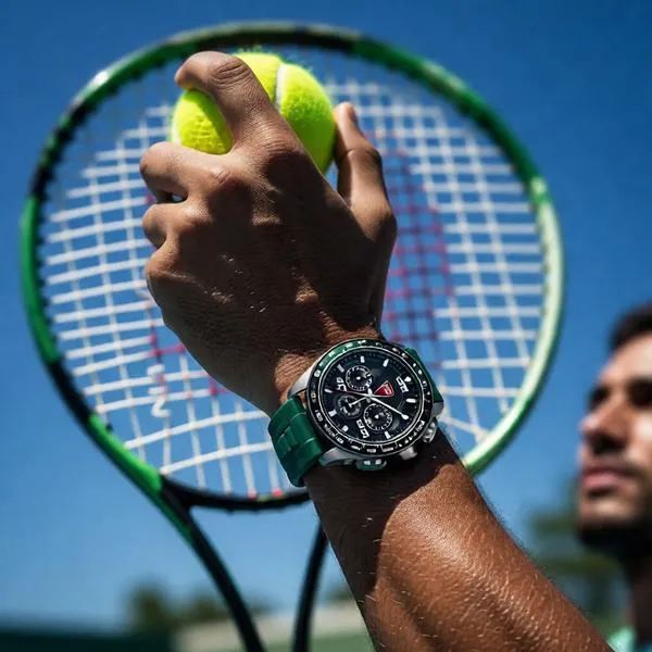 Athlete preparing to serve on a tennis court with a sports watch prominently displayed on the wrist against a bright blue sky.
