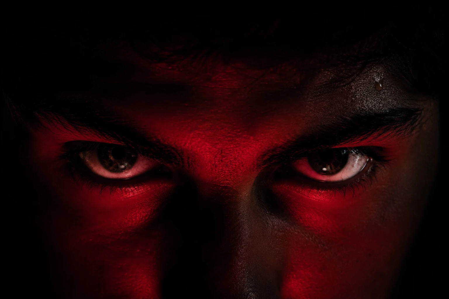 Dramatic close-up of intense eyes emerging from darkness under red directional lighting