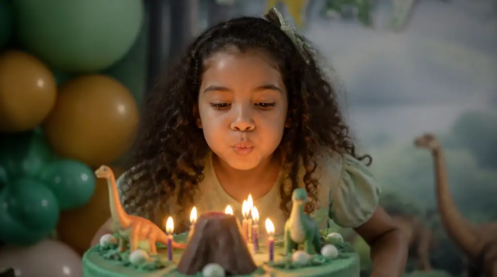 Criança brasileira soprando velinhas de bolo temático em festa ao ar livre