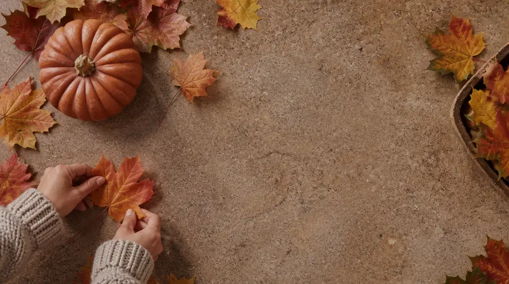 Overhead autumn still life with maple leaves and a small pumpkin on a warm earthy surface with open space for text.