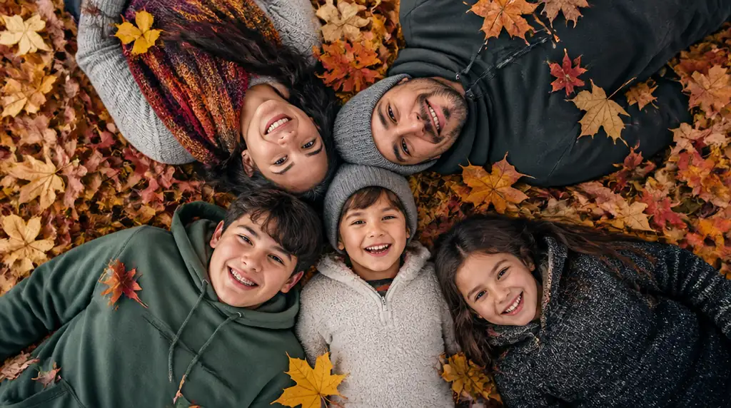 Family lying together in a colorful pile of autumn leaves and smiling up at the camera.
