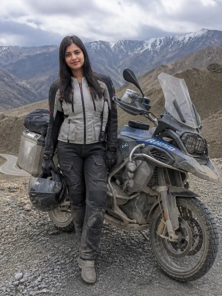 Adventure rider standing beside a dusty touring motorcycle at a rugged mountain overlook after a long road journey.