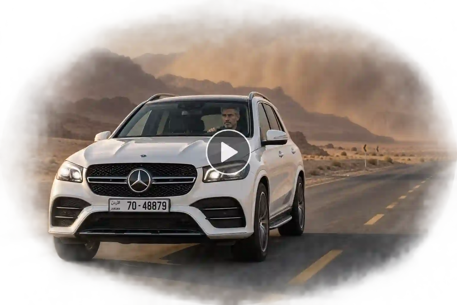 Mercedes driving across a desert highway with blowing sand and rocky formations in the distance