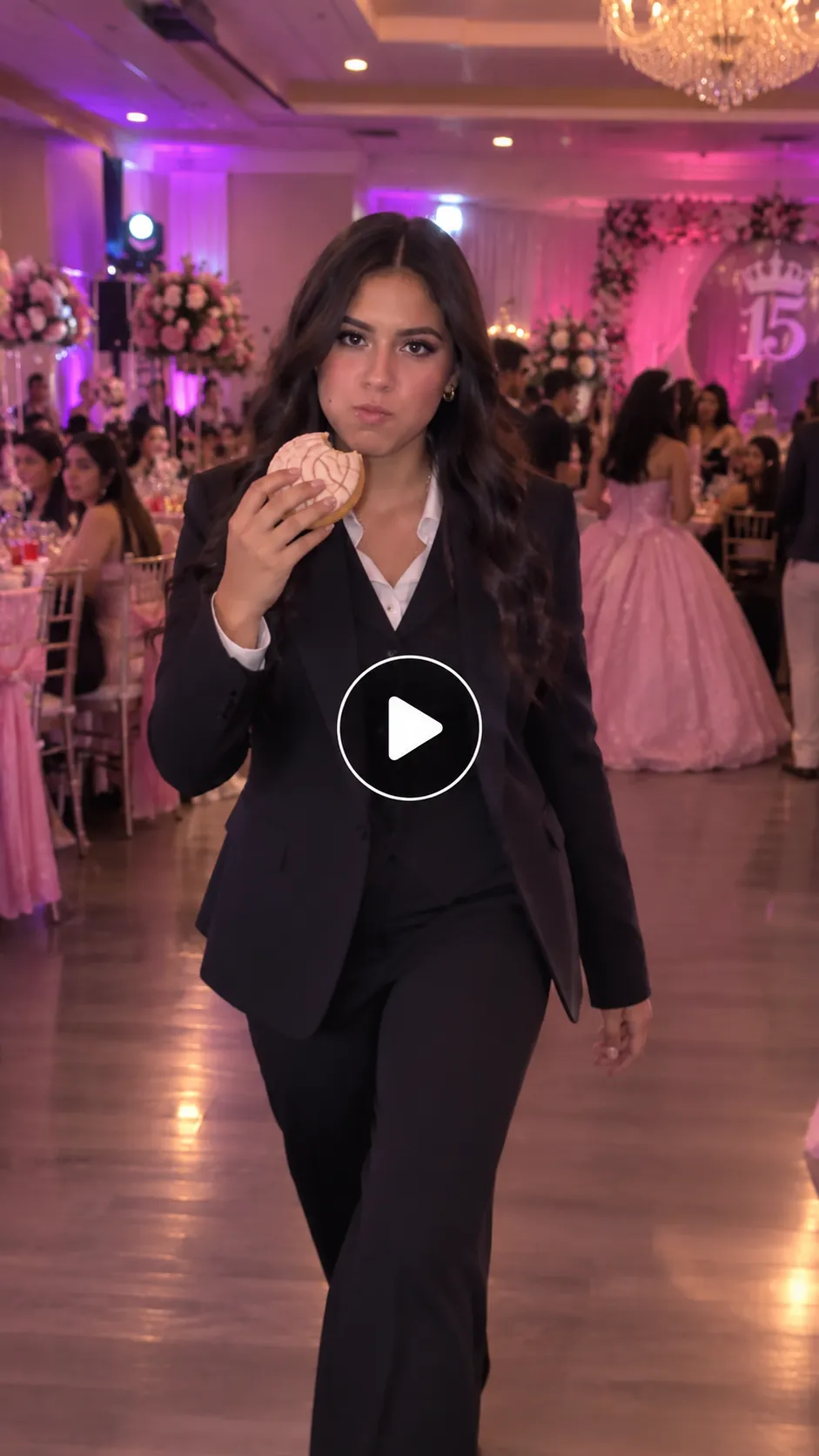 A woman in a black suit eats a Mexican concha at a pink and purple quinceañera party, with a transparent play button in the center.