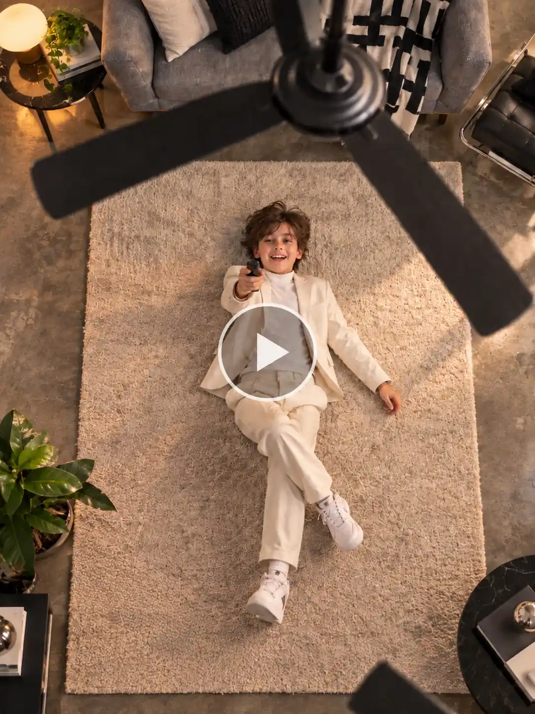 AI ceiling fan trend showing a woman lying on a patterned rug, pointing a remote at a spinning ceiling fan.