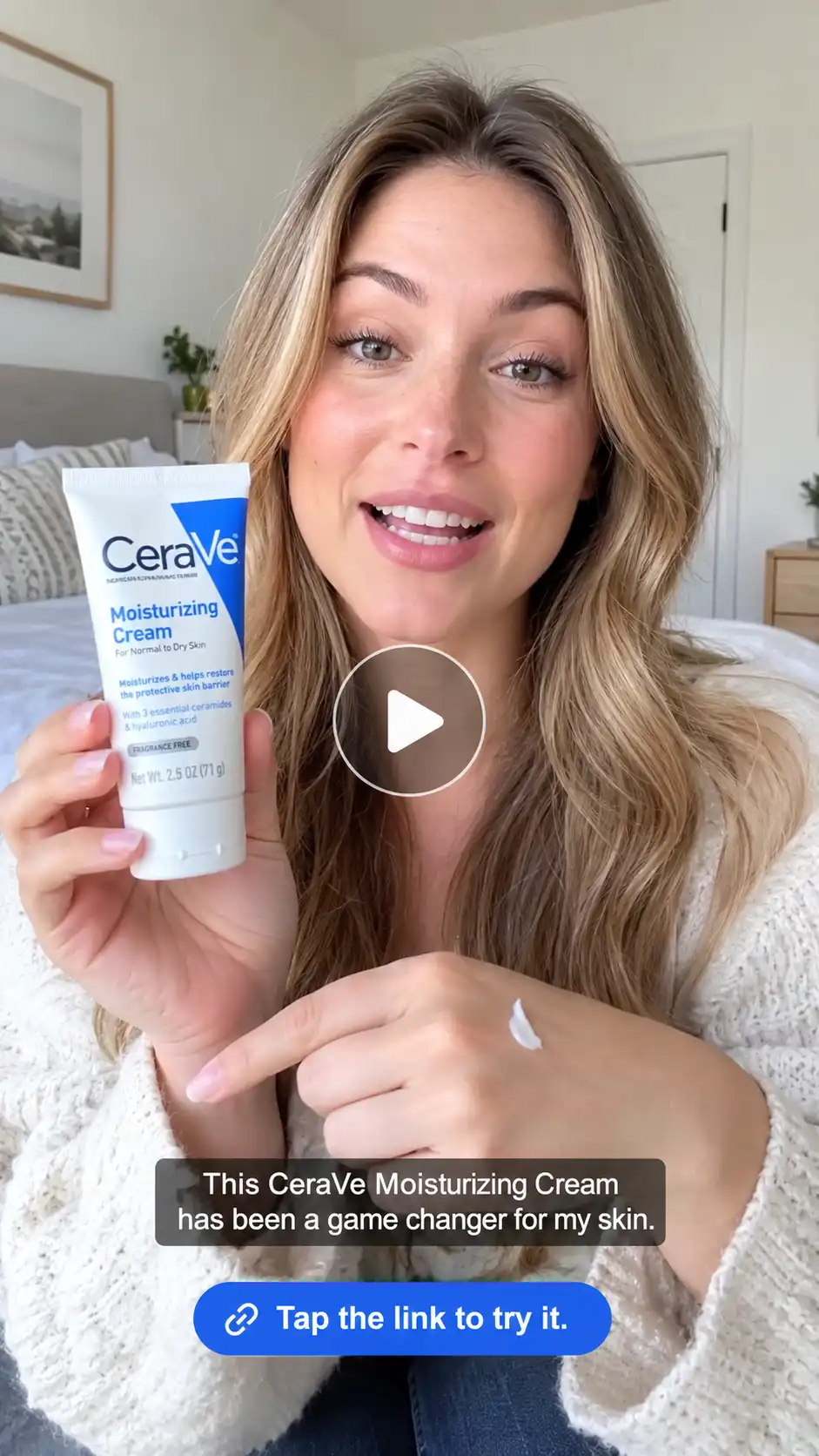 An American woman showcasing CeraVe moisturizing cream and applying a small amount to her hand in a bright bedroom, with a centered play button and product review captions.